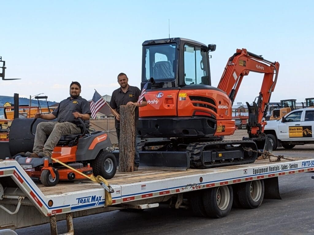 Black Hills Equipment Rentals team delivering a Kubota mini excavator and Husqvarna mower on a flatbed trailer in Spearfish, SD.